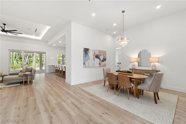 dining space with ceiling fan, light wood-type flooring, and a tray ceiling