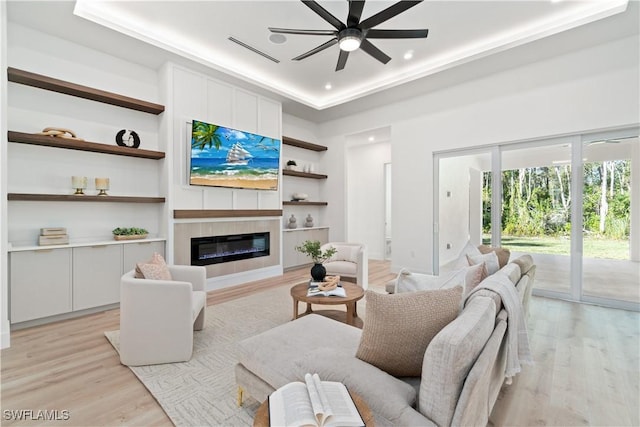 living room with light hardwood / wood-style flooring, built in features, ceiling fan, and a tray ceiling