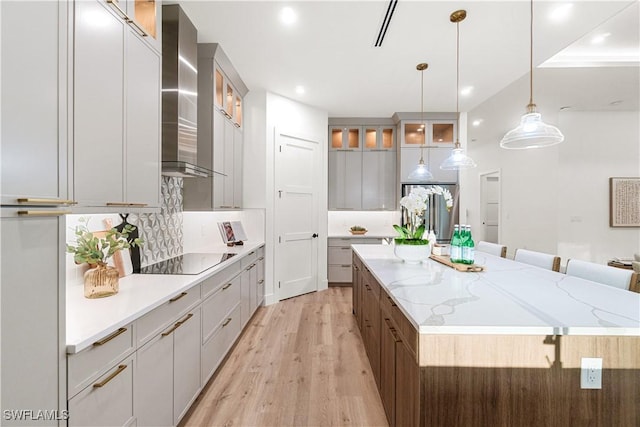 kitchen featuring black electric stovetop, light wood-style flooring, decorative backsplash, wall chimney range hood, and a large island