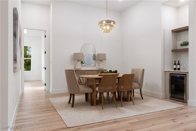 dining area with a chandelier, beverage cooler, light wood-style floors, and a dry bar