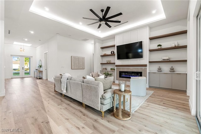 living area with a ceiling fan, french doors, light wood finished floors, and a tray ceiling