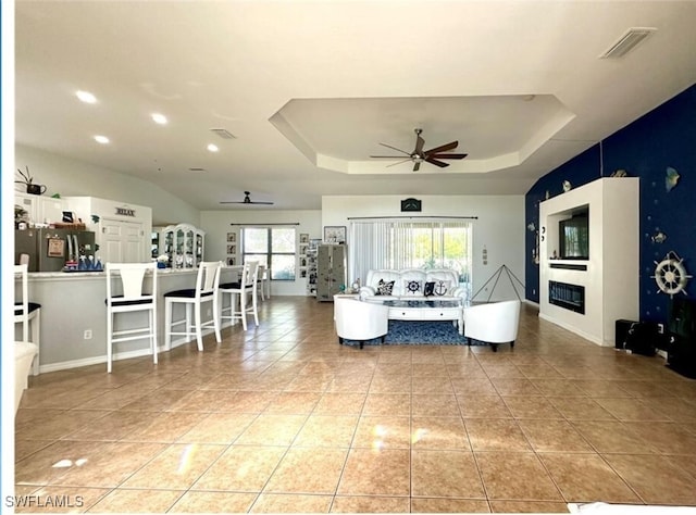 living room with a raised ceiling, light tile patterned floors, and ceiling fan