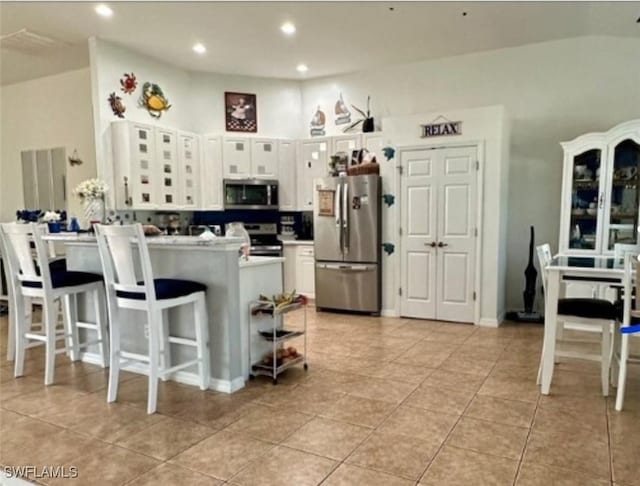 kitchen with light tile patterned flooring, appliances with stainless steel finishes, white cabinets, a kitchen breakfast bar, and kitchen peninsula