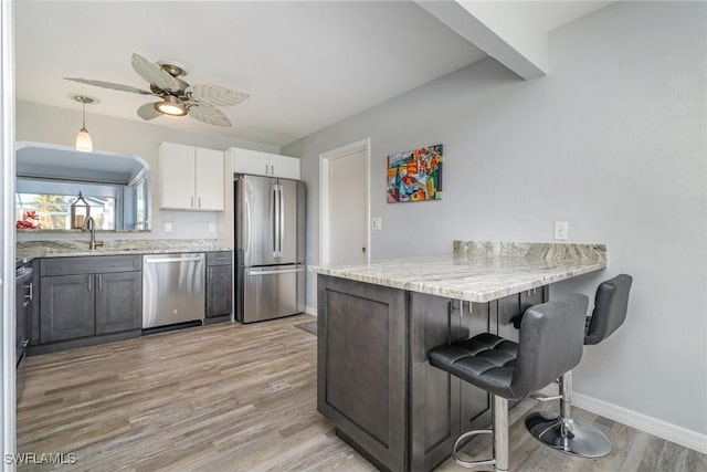 kitchen featuring sink, a breakfast bar area, stainless steel appliances, light stone countertops, and white cabinets