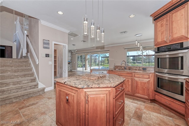 kitchen featuring sink, double oven, hanging light fixtures, ornamental molding, and a kitchen island