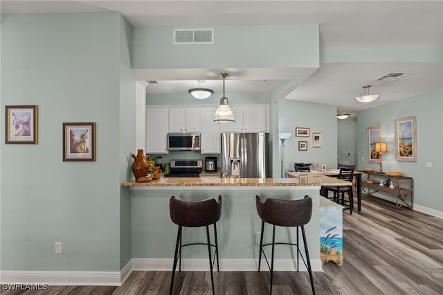 kitchen featuring a breakfast bar area, appliances with stainless steel finishes, white cabinetry, decorative light fixtures, and kitchen peninsula