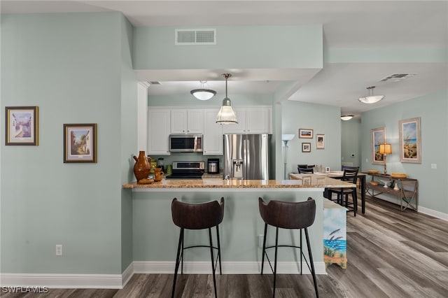 kitchen featuring visible vents, a breakfast bar area, dark wood-type flooring, white cabinetry, and appliances with stainless steel finishes