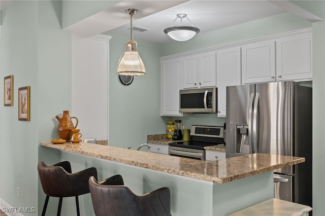 kitchen featuring a breakfast bar area, light stone counters, pendant lighting, stainless steel appliances, and white cabinets