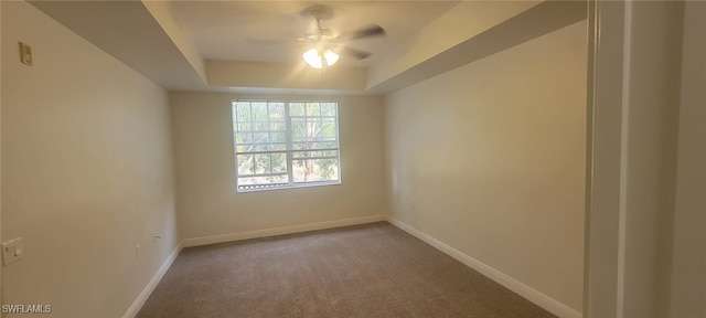 empty room featuring a tray ceiling, ceiling fan, and carpet