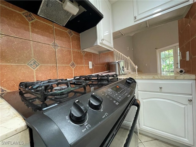 kitchen featuring black gas range, range hood, and white cabinets