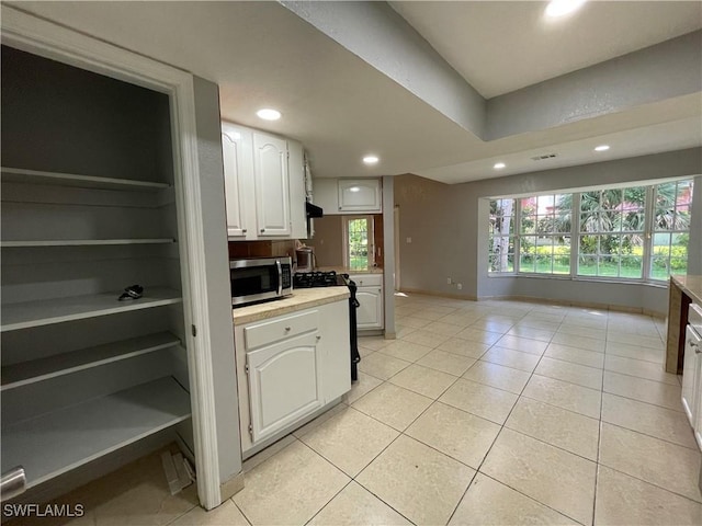 kitchen featuring white cabinetry, a healthy amount of sunlight, light tile patterned flooring, and black range