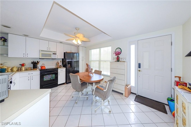 kitchen with black appliances, light tile patterned floors, a tray ceiling, ceiling fan, and white cabinets