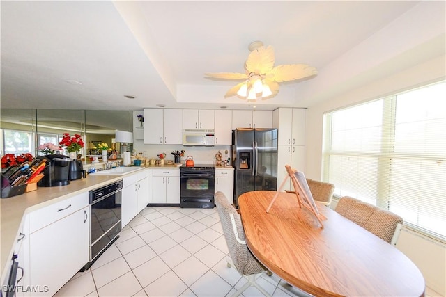 kitchen with sink, black appliances, light tile patterned floors, a tray ceiling, and white cabinets