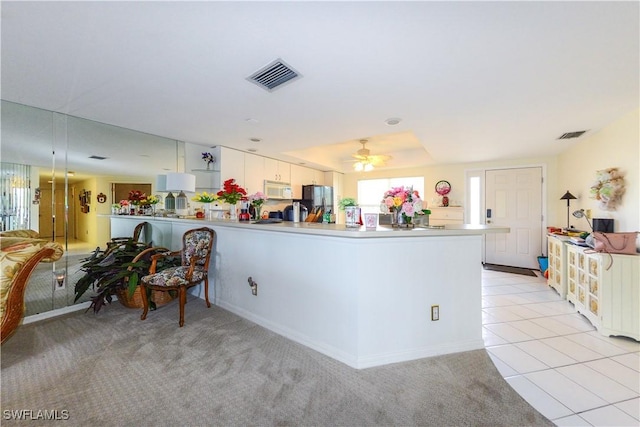 kitchen featuring light tile patterned floors, ceiling fan, white cabinets, black fridge, and kitchen peninsula