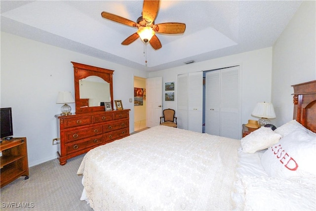 bedroom featuring a raised ceiling, light colored carpet, and ceiling fan