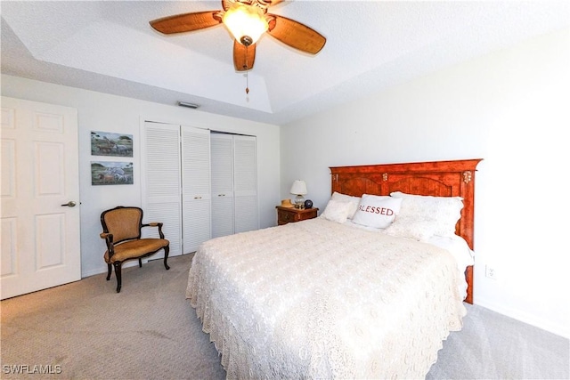 carpeted bedroom with lofted ceiling, a tray ceiling, ceiling fan, and a closet