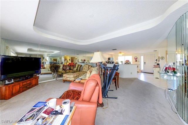 living room featuring ceiling fan, light colored carpet, a textured ceiling, and a tray ceiling