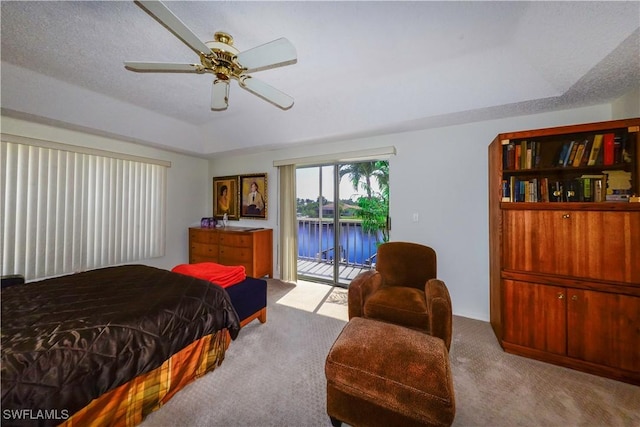 bedroom with a water view, a tray ceiling, a textured ceiling, access to outside, and light colored carpet