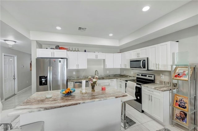 kitchen featuring appliances with stainless steel finishes, light stone countertops, a kitchen island, and white cabinets