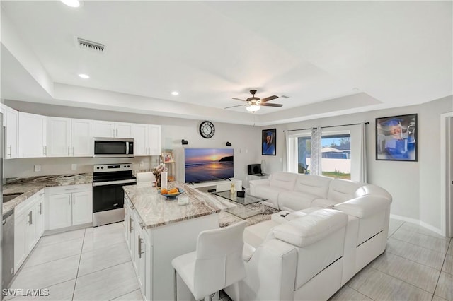 kitchen with light tile patterned floors, stainless steel appliances, a tray ceiling, white cabinets, and a kitchen island