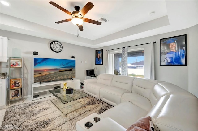 living room with a raised ceiling and ceiling fan