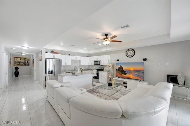 tiled living room featuring a raised ceiling and ceiling fan