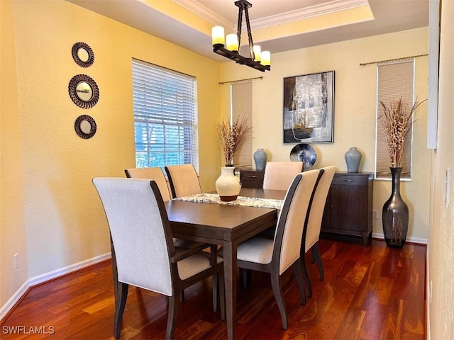 dining space featuring dark wood-type flooring, ornamental molding, a raised ceiling, and an inviting chandelier