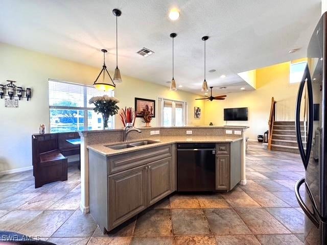 kitchen featuring sink, light stone counters, black appliances, a center island with sink, and decorative light fixtures