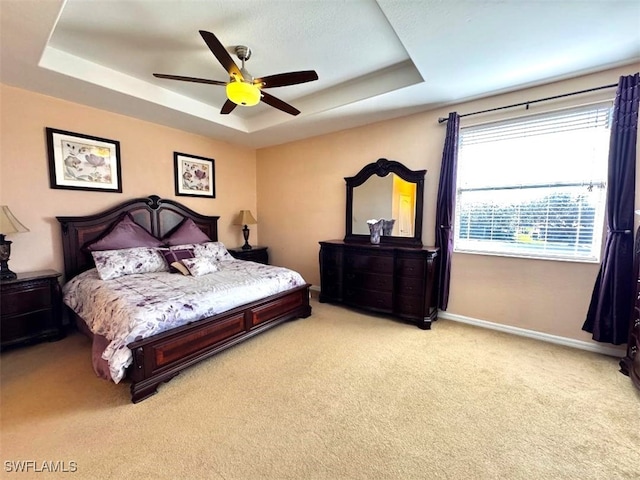 bedroom featuring a tray ceiling, light colored carpet, and ceiling fan