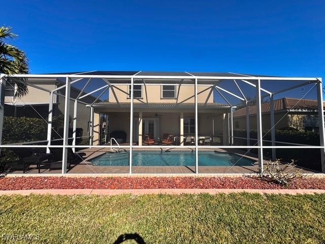 rear view of house featuring ceiling fan, a patio area, glass enclosure, and a lawn