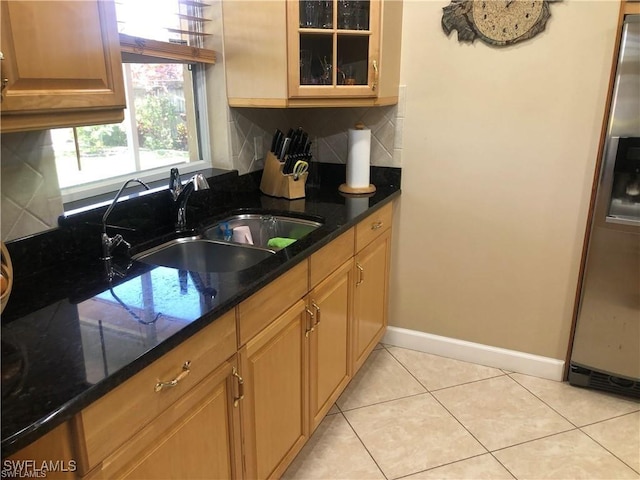 kitchen with light tile patterned flooring, sink, stainless steel fridge, dark stone counters, and backsplash