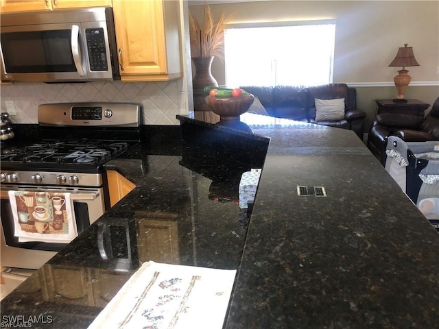 kitchen featuring backsplash, stainless steel appliances, dark stone counters, and light brown cabinets