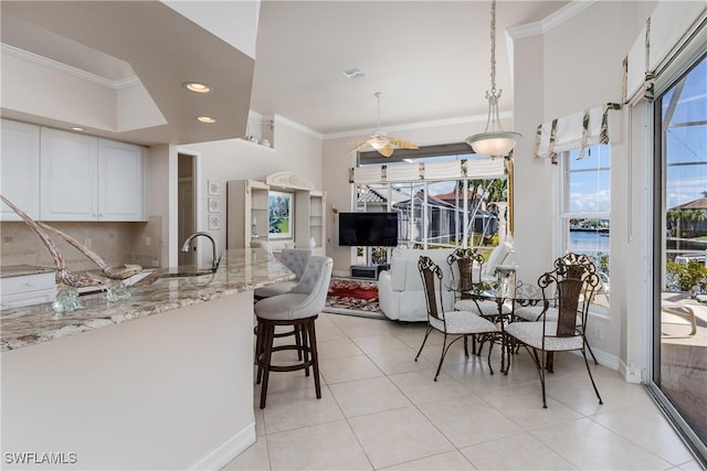 kitchen with pendant lighting, white cabinetry, crown molding, and light stone countertops