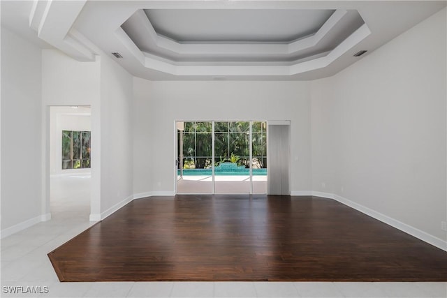 unfurnished room with a tray ceiling, light hardwood / wood-style flooring, and a towering ceiling