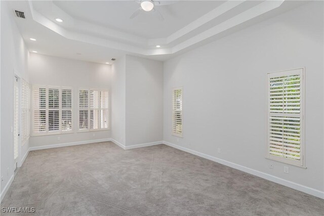 spare room with a tray ceiling, light colored carpet, ceiling fan, and a towering ceiling