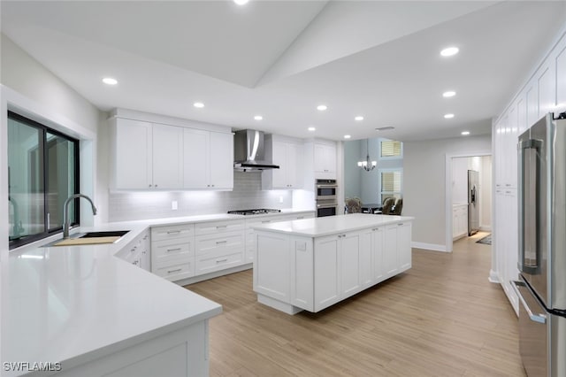 kitchen featuring wall chimney exhaust hood, sink, a center island, stainless steel appliances, and white cabinets