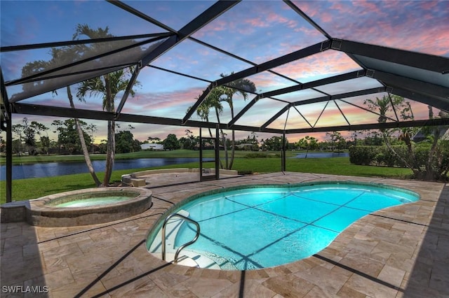 pool at dusk featuring a patio, an in ground hot tub, a yard, glass enclosure, and a water view