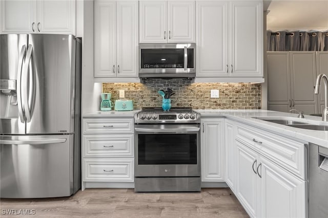 kitchen with sink, appliances with stainless steel finishes, white cabinetry, tasteful backsplash, and light hardwood / wood-style floors