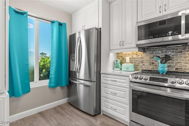 kitchen with appliances with stainless steel finishes, white cabinets, decorative backsplash, a healthy amount of sunlight, and light wood-type flooring