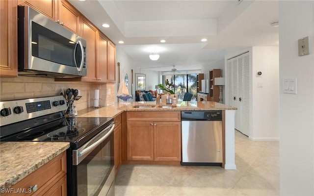 kitchen with appliances with stainless steel finishes, kitchen peninsula, sink, and a raised ceiling