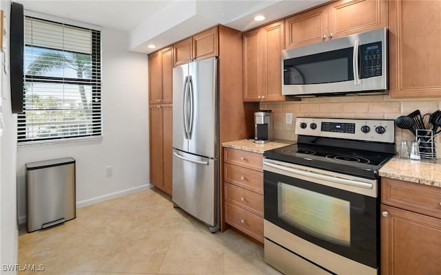 kitchen featuring light stone countertops, decorative backsplash, stainless steel appliances, and light tile patterned floors