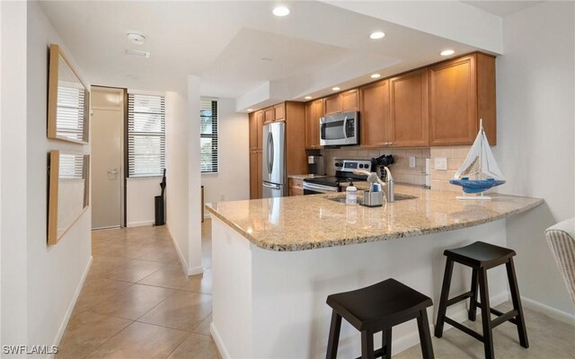 kitchen featuring appliances with stainless steel finishes, a breakfast bar, light stone counters, and kitchen peninsula