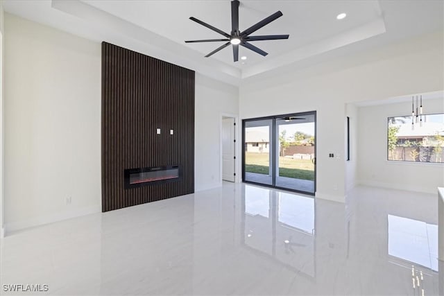 unfurnished room with ceiling fan, a healthy amount of sunlight, a tray ceiling, and a towering ceiling