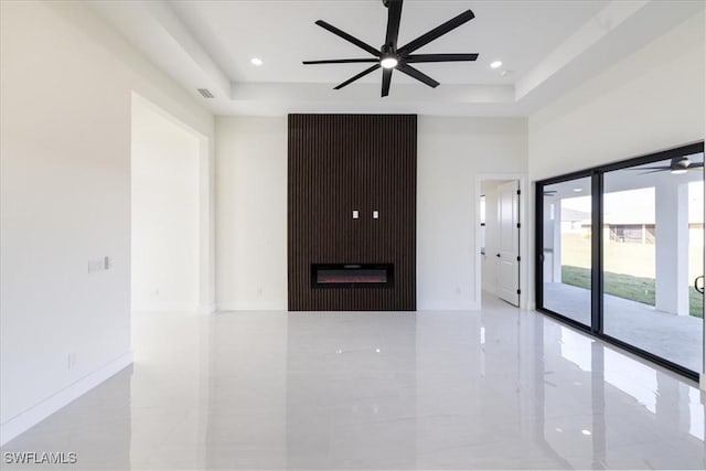 unfurnished living room featuring ceiling fan, a large fireplace, a tray ceiling, and a high ceiling