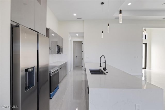 kitchen featuring appliances with stainless steel finishes, sink, a large island with sink, hanging light fixtures, and light stone counters