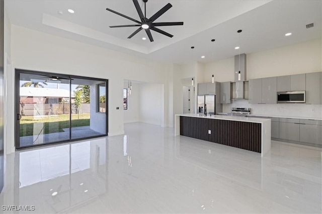 kitchen featuring appliances with stainless steel finishes, a high ceiling, a large island, a raised ceiling, and wall chimney range hood