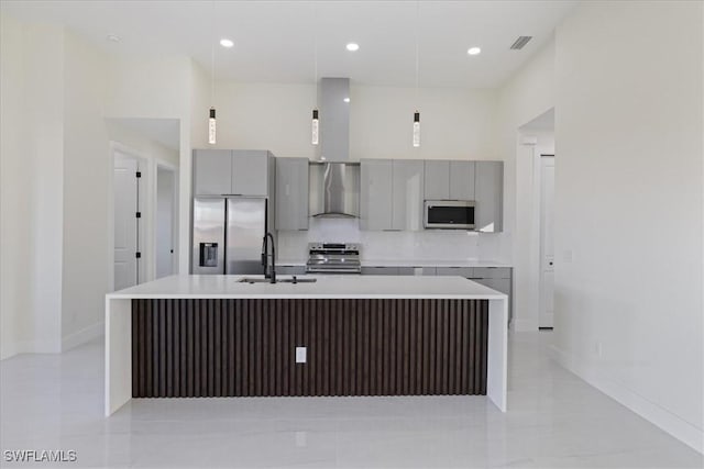 kitchen with pendant lighting, appliances with stainless steel finishes, sink, and wall chimney range hood