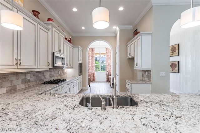 kitchen featuring arched walkways, light stone counters, a sink, hanging light fixtures, and appliances with stainless steel finishes