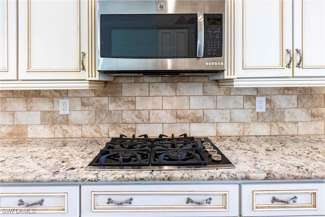 kitchen with light stone countertops, appliances with stainless steel finishes, and backsplash