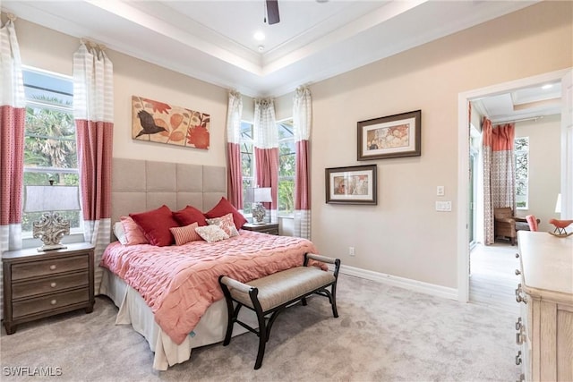 bedroom featuring light carpet, multiple windows, a raised ceiling, and baseboards